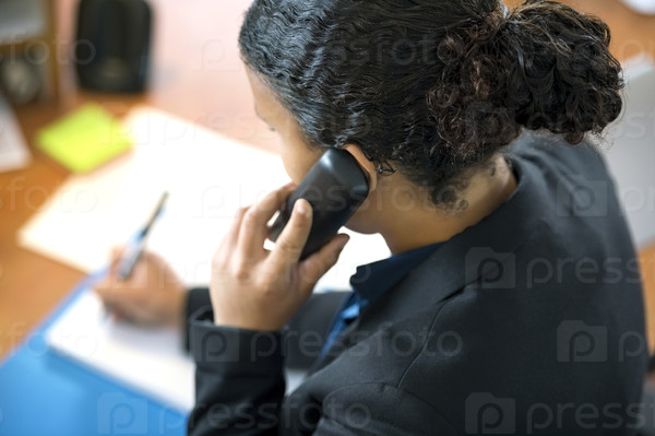 High angle view of receptionist using cordless phone while writing at counter in office