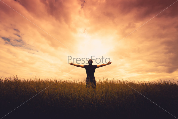 silhouette of man standing in a field at sunset