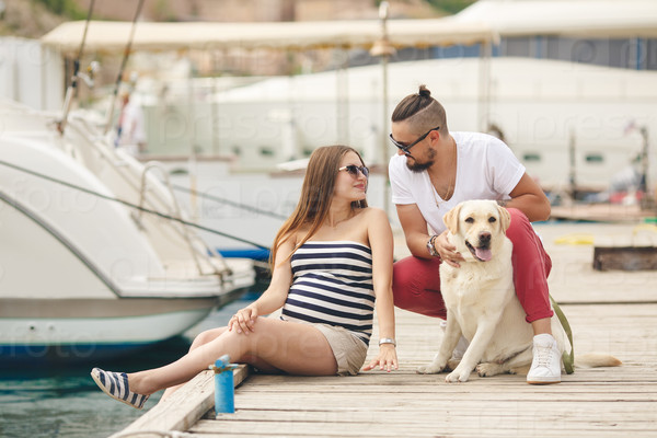 Young pregnant Family with dog Outdoors by the sea. with yachts on the background. Happy family resting outdoors in summer. Family with dog