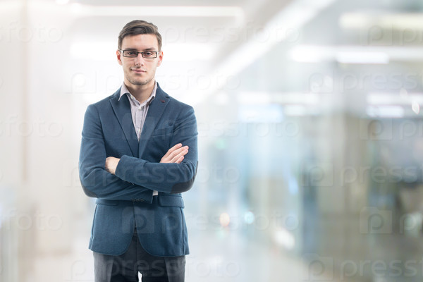 Young handsome businessman wearing glasses in the office and standing alone hands crossed