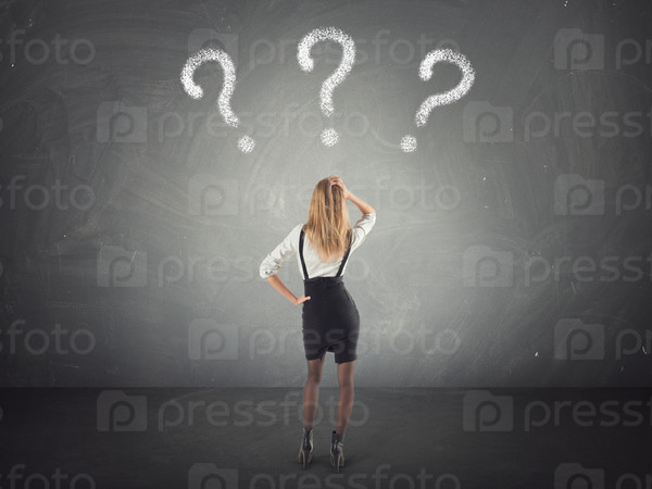 Confused businesswoman looking at questions mark in the wall