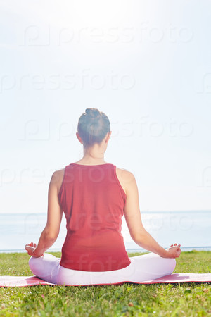 Meditating woman sitting on green grass by the seaside