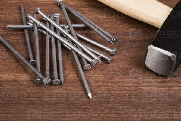 Hammer with pile of nails on brown wood table, stock photo