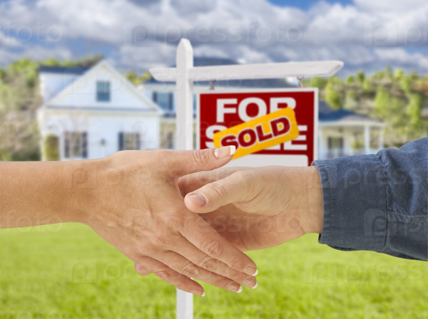 Man and Woman Shaking Hands in Front of a Beautiful New House and Sold For Sale Real Estate Sign.