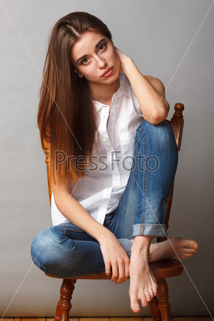 beautiful brunette fashion model posing at studio, sitting on chair with feet