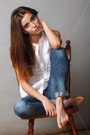 beautiful brunette fashion model posing at studio, sitting on chair with feet