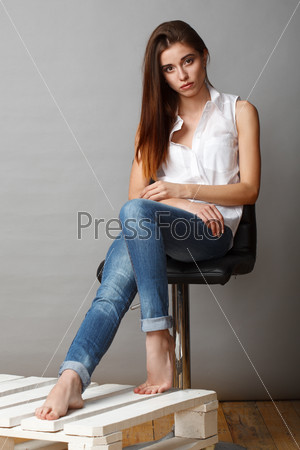 beautiful brunette fashion model posing at studio, sitting on chair, hands on knees