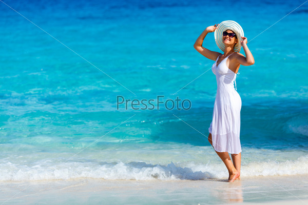 Young woman in a white dress walking on the tropical beautiful beach, stock photo