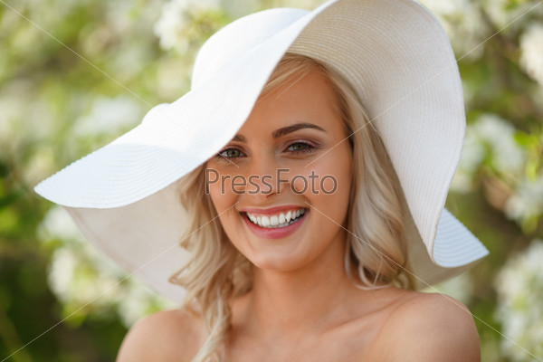 beautiful blonde woman head and shoulders portrait in a flowered spring garden, wearing big white hat