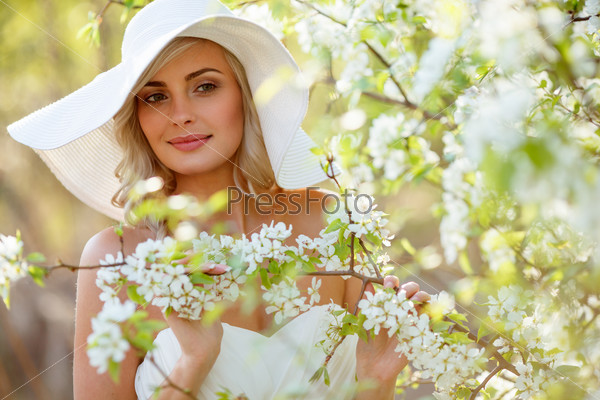 beautiful blonde woman head and shoulders portrait in a flowered spring garden, wearing big white hat