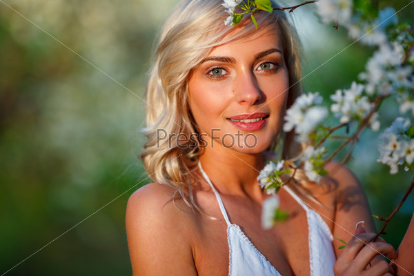Beautiful blonde woman portrait in a flowered spring garden during sunset, stock photo