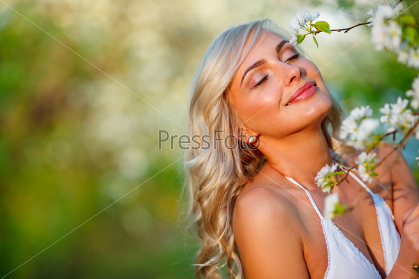 beautiful blonde woman portrait in a flowered spring garden during sunset