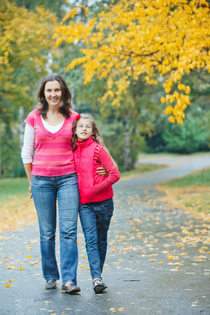 Cute girl with her mother walking in the autumn park. Rain, yellow leaves, tree.
