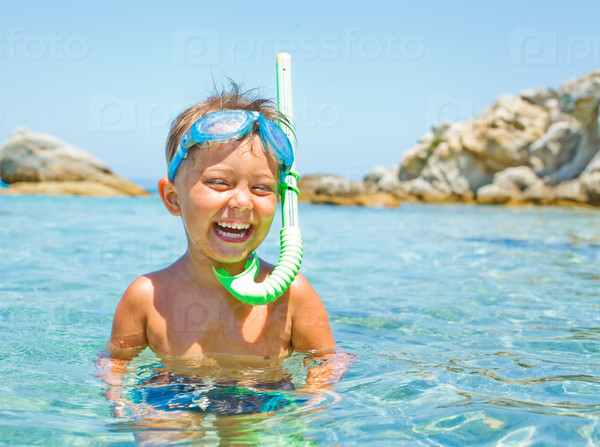 Cute boy in swimming goggles and snorkel swimming in the transparent sea