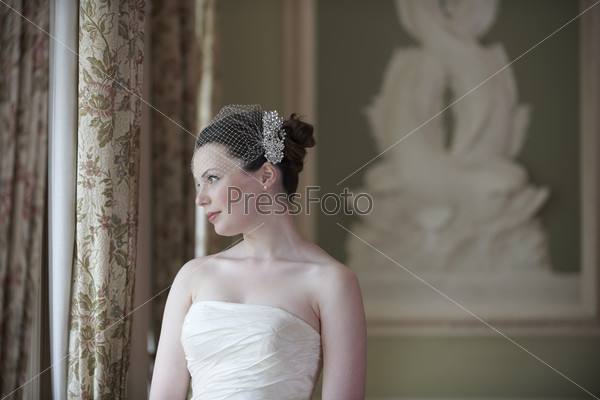 Pretty bride looking out of window and smiling on her wedding day