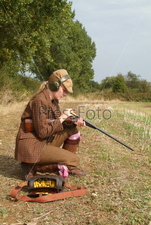 Young female hunter loading a gun on the field