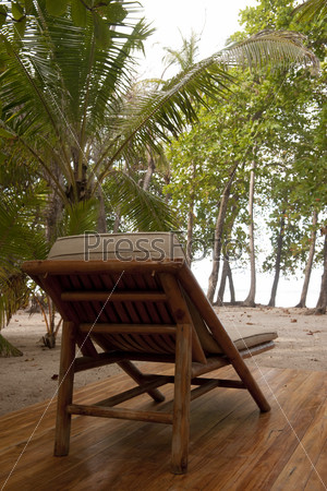 Reclining wood lounge chair on a wooden deck facing jungle trees