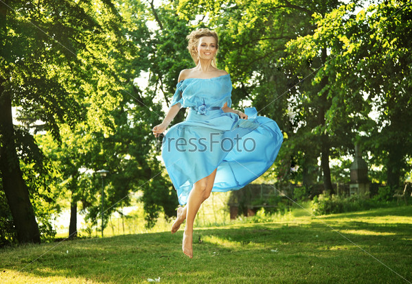 Young woman in blue dress jumping over green grass