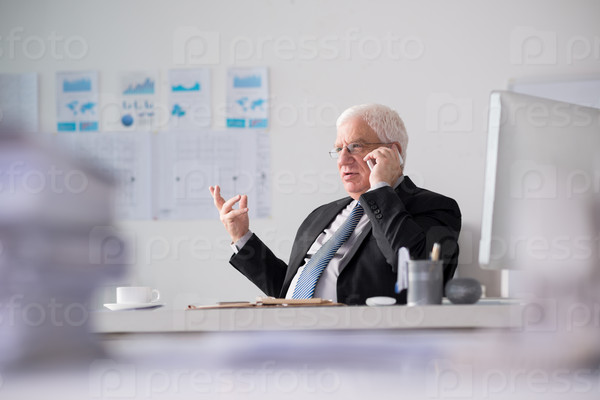 Serious aged businessman talking on the phone in his office