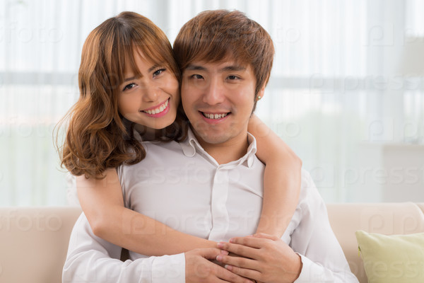 Beautiful Vietnamese girl hugging her boyfriend from behind, both smiling at the camera