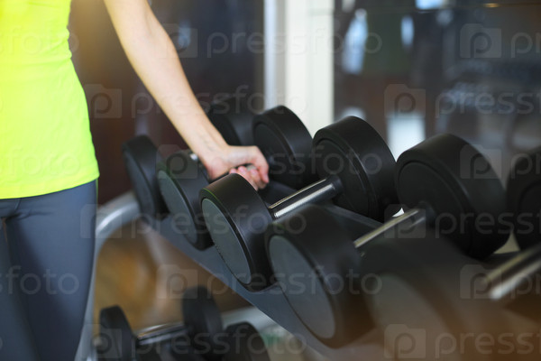 Fitness young woman with barbells on gym background