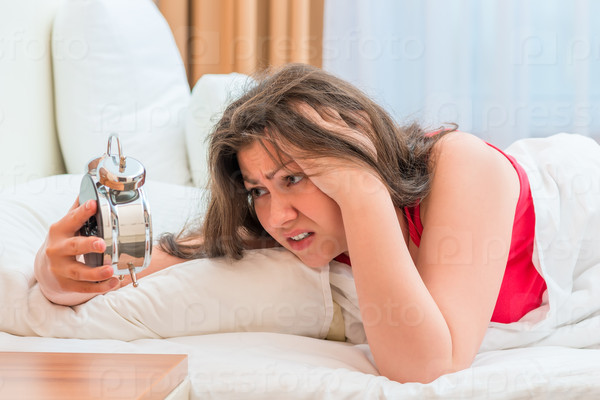 Woman looks at an alarm clock, can not to fall asleep, stock photo