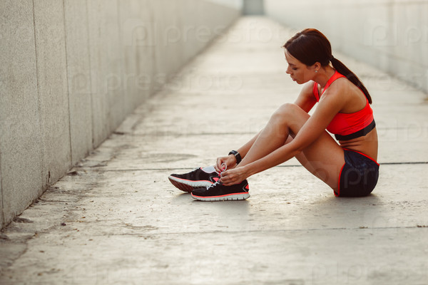 Brunette runner woman sitting on the ground and tie laces, sunset time, evening workout, stock photo