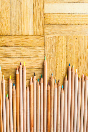 Bunch of different colours pencil with wooden body on parquet background vertical frame