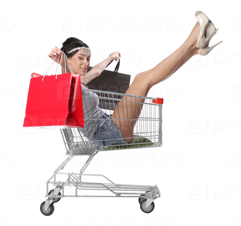 Pretty brunette woman sits in an empty shopping trolley with a shopping bags