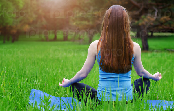 Young girl practicing yoga in nature in the woods on a background of green trees and grass.Woman covers a ray of sunshine at sunset