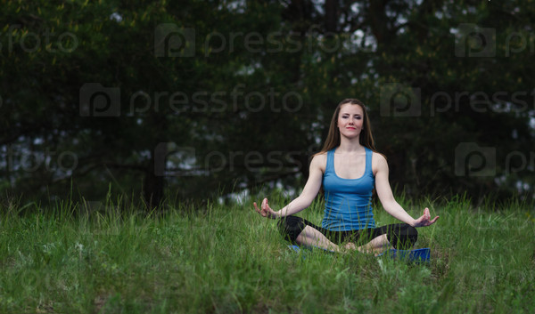 Young girl practicing yoga in nature in the woods on a background of green trees and grass. lotus Pose