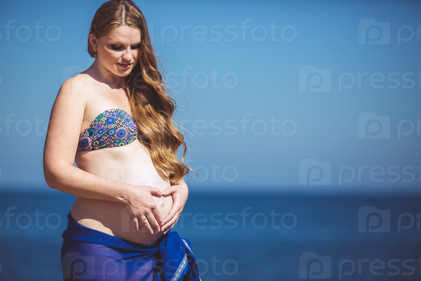 Portrait of pregnant beautiful woman on the seashore opposite blue sea and blue sky. Outdoors.