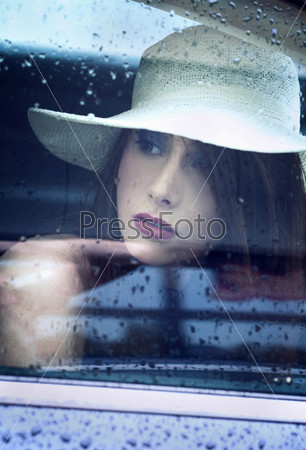 Young attractive woman looking through window after rain