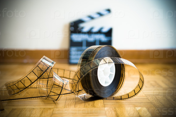 35 mm cinema film reel and out of focus movie clapper board in background on wooden floor