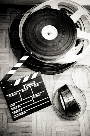 Cinema movie clapper board and film reel on wooden floor in vintage black and white vertical frame
