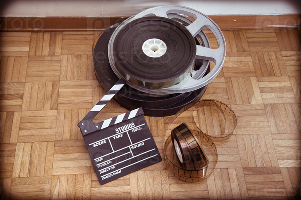 Cinema movie clapper board and 35 mm film reel on wooden floor vintage color effect