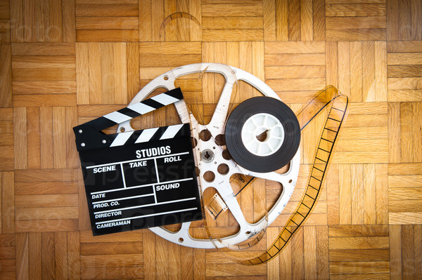 Cinema movie clapper board with 35 mm filmstrip and reel on wooden floor