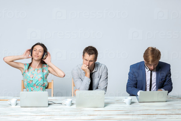 Business team working together at office on light gray background. all working on laptops. girl in headphones enjoying the music