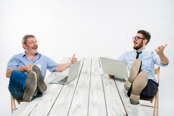The two businessmen with legs over table working on laptops