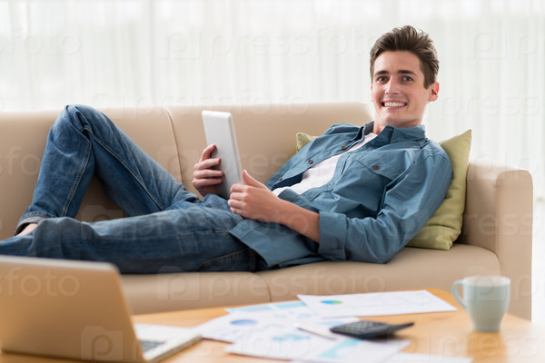 Happy excited guy with a tablet computer lying on the sofa