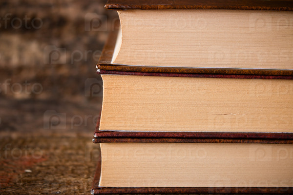 three brown books in a stack vertically on wooden background close-up page