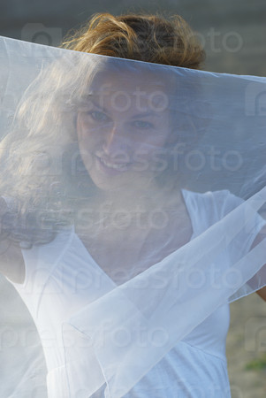 Young attractive woman in white dress and holding white scarf on beach