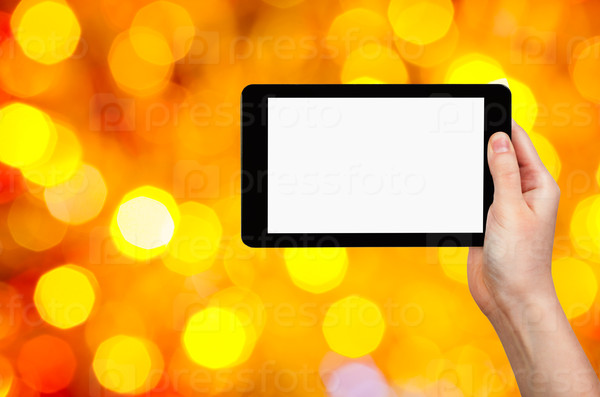 christmas party concept - hand with tablet pc with cut out screen on background from yellow and red shimmering Christmas lights of electric garlands on Xmas tree