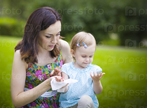 Mother using wet wipes for her daughter on white park background