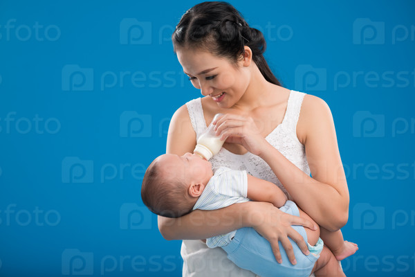 Happy young mother feeding her little son with milk bottle