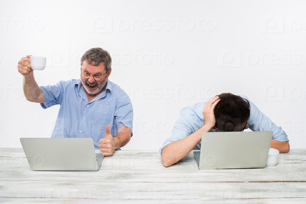 The two colleagues working together at office on white background. The old man getting good news. the young man is upset. concept of competition in business and jealousy, stock photo
