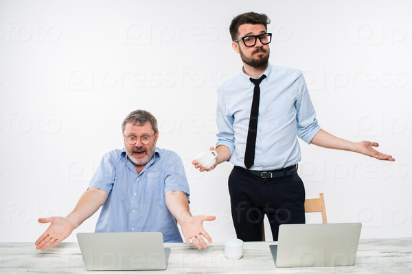 The two colleagues working together at office on white  background. Old man sitting at the table with computers and both shruging aside as if to saying -It happened