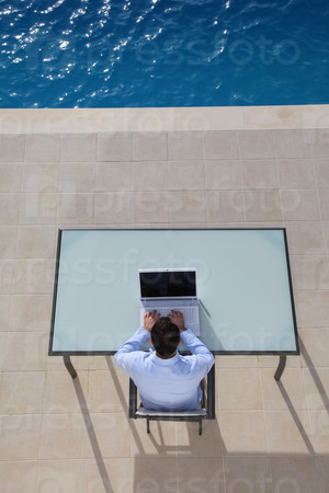 View from above of man using computer by swimming-pool