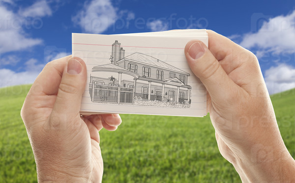 Male Hands Holding Stack of Paper With House Drawing Over Empty Grass Field and Sky.
