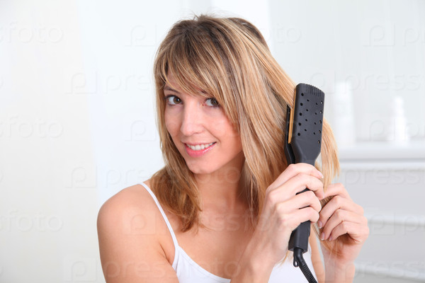 Beautiful blond woman straightening her hair